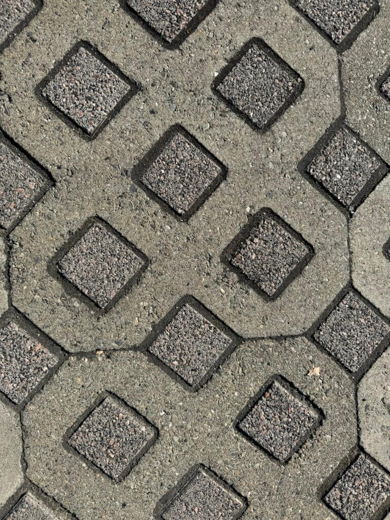 Close-up of a textured surface featuring interlocking hexagonal and diamond-shaped patterns with gray and dark gray tones, highlighting cracks and shadows in concrete material.