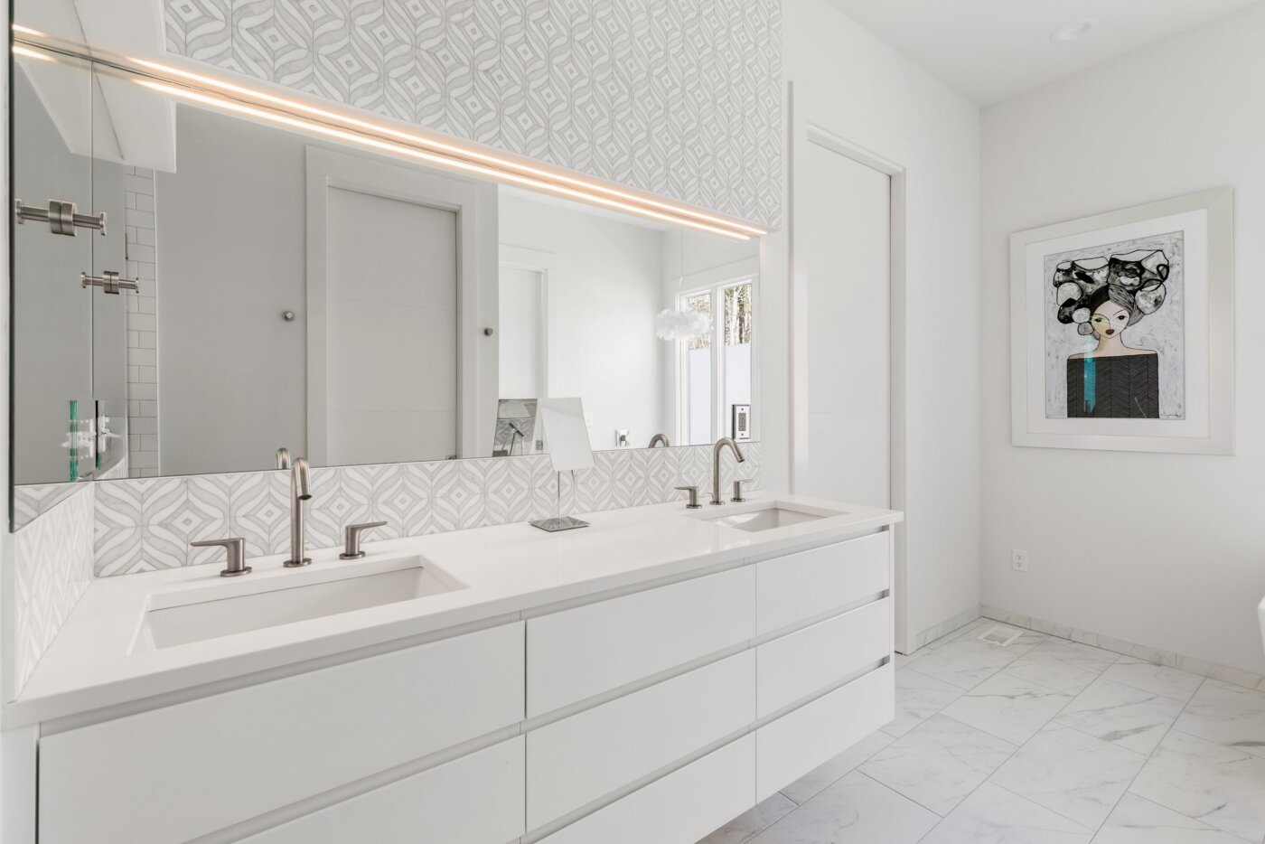 Modern white bathroom with double sinks, large mirror, geometric tile backsplash, and framed abstract art on the wall. Light fills the space, highlighting clean lines and minimalistic decor.