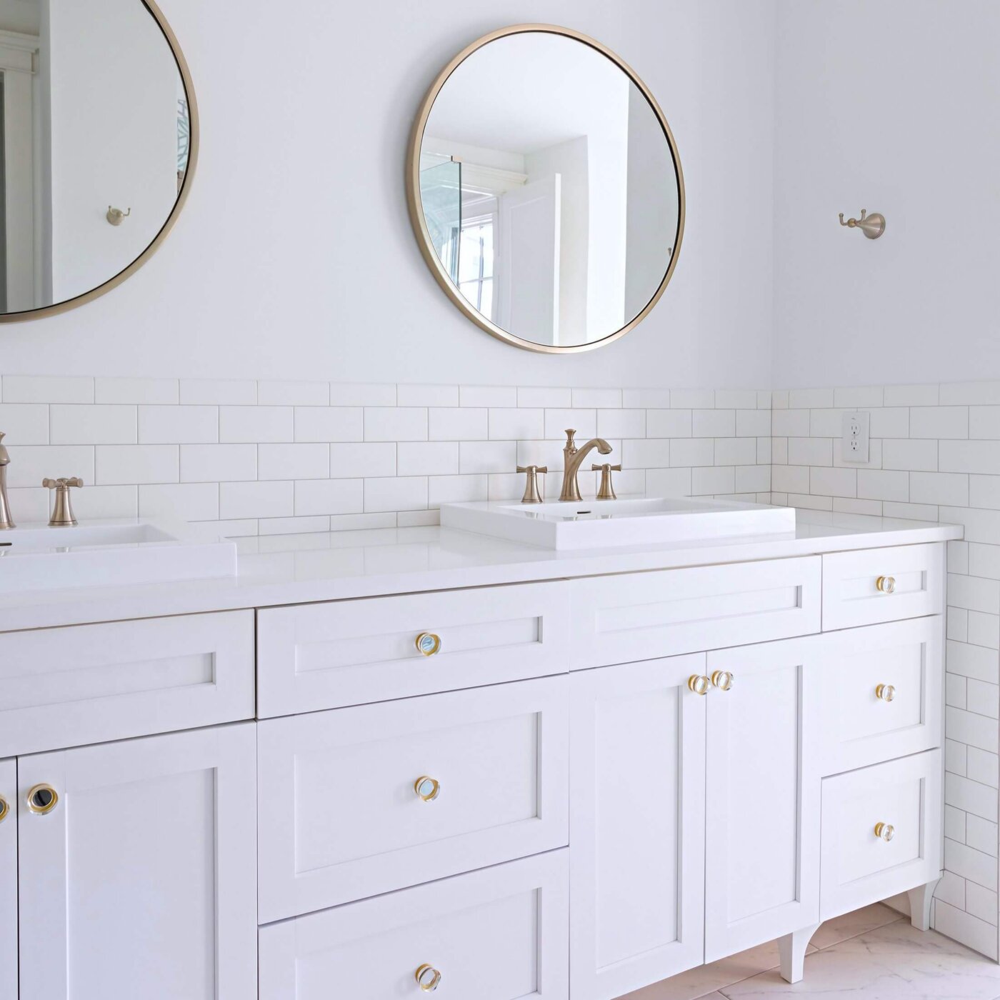 Modern bathroom with two round mirrors, white double vanity, gold fixtures, and white tile backsplash. The design is minimalistic and bright, with clean lines and simple decor.